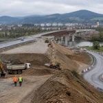 Stavenisko rýchlostnej cesty pri Banskej Bystrici so štrkovými násypmi, provizórnou obchádzkou a pracovníkmi v diaľke.